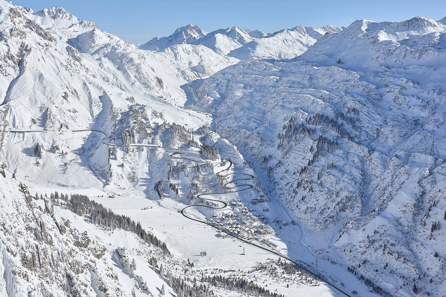 Eine kurvenreiche Straße schlängelt sich durch ein weites, schneebedecktes Tal in den Bergen.