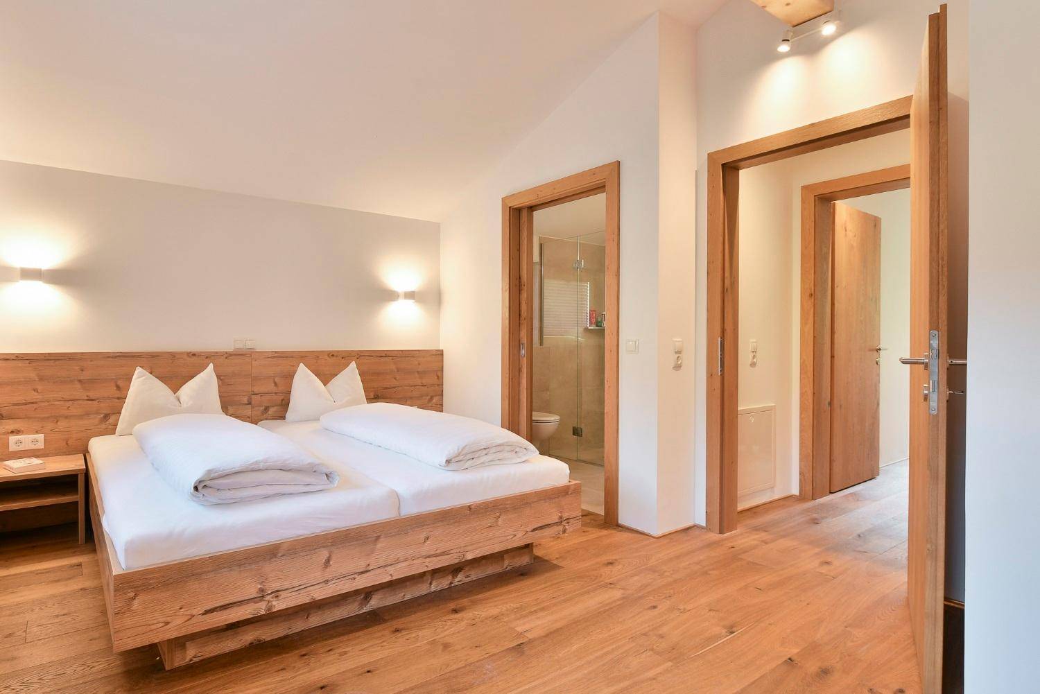 Schlafzimmer mit Holzboden und direktem Zugang zu einem modernen Badezimmer.