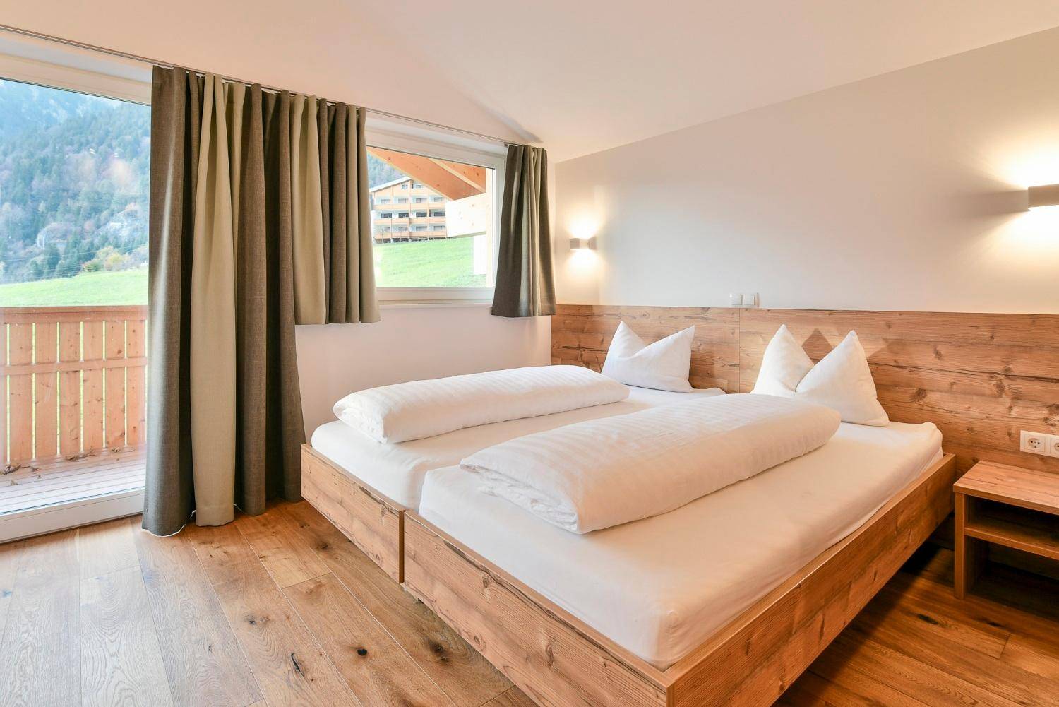 Helles Schlafzimmer mit Holzboden, Doppelbett und großem Fenster mit Bergblick.