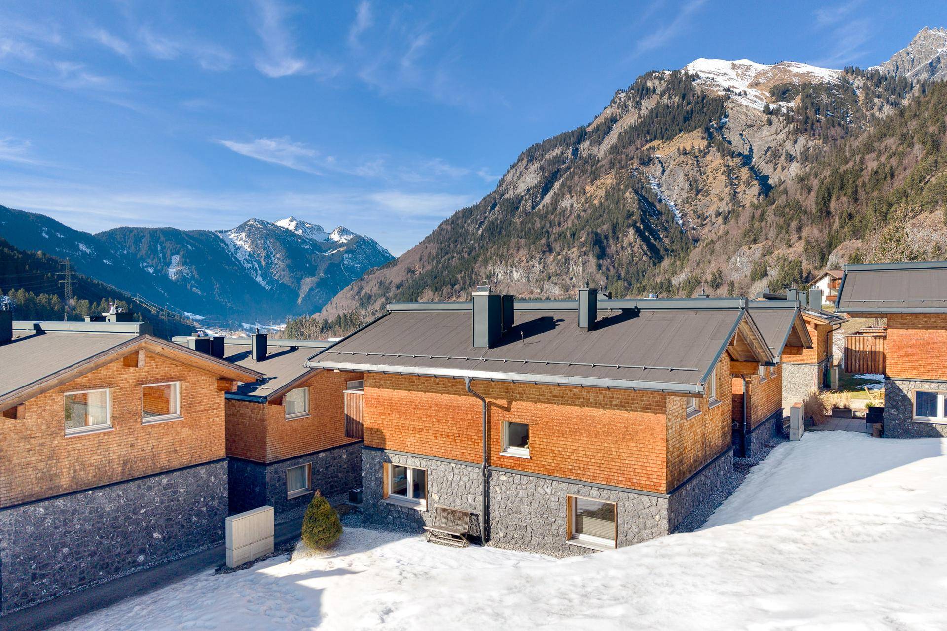 Mehrere moderne Chalets in einer verschneiten Berglandschaft mit klarem Himmel und alpiner Architektur.