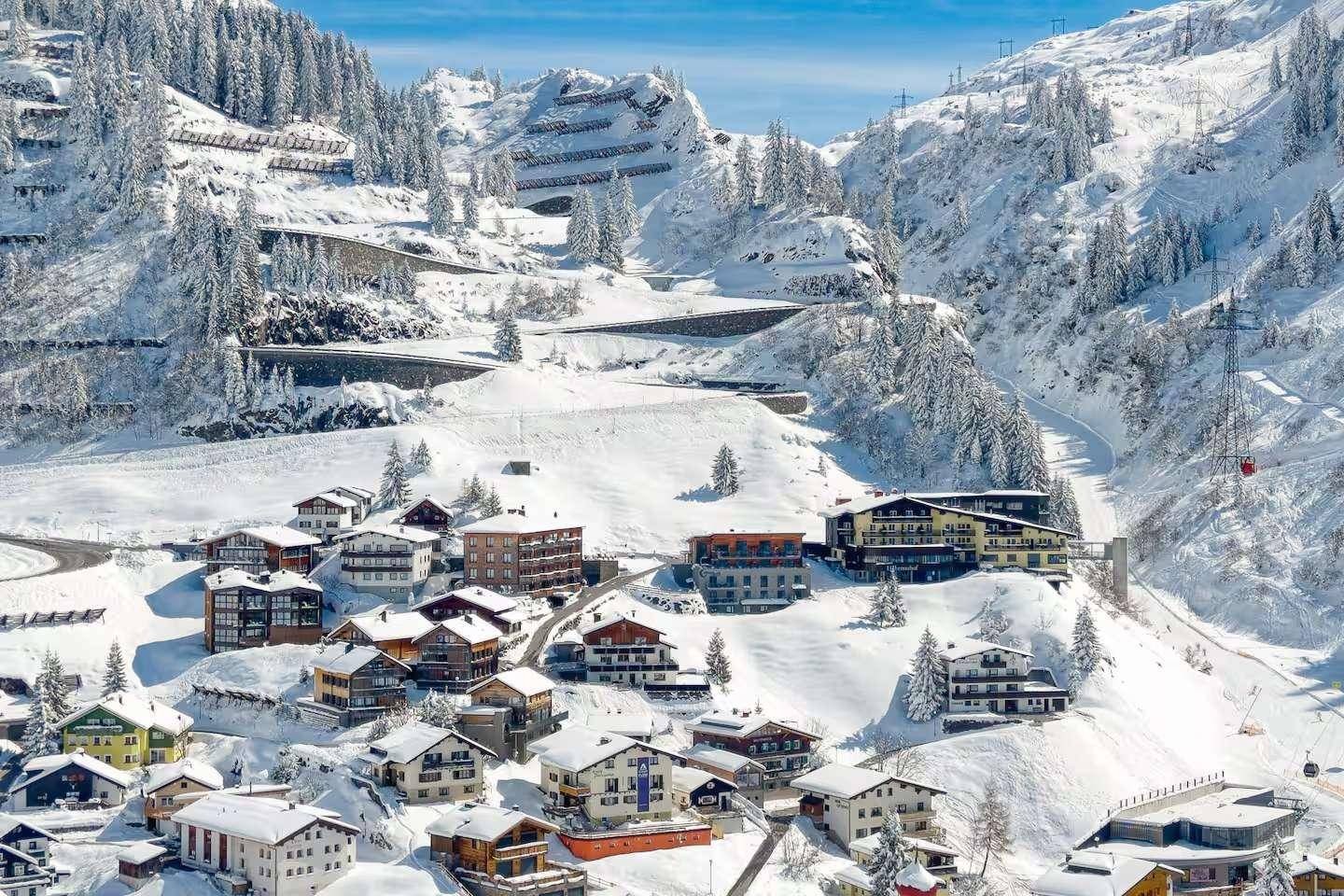 Panoramablick auf ein verschneites Dorf in den Alpen mit Serpentinenstraßen.