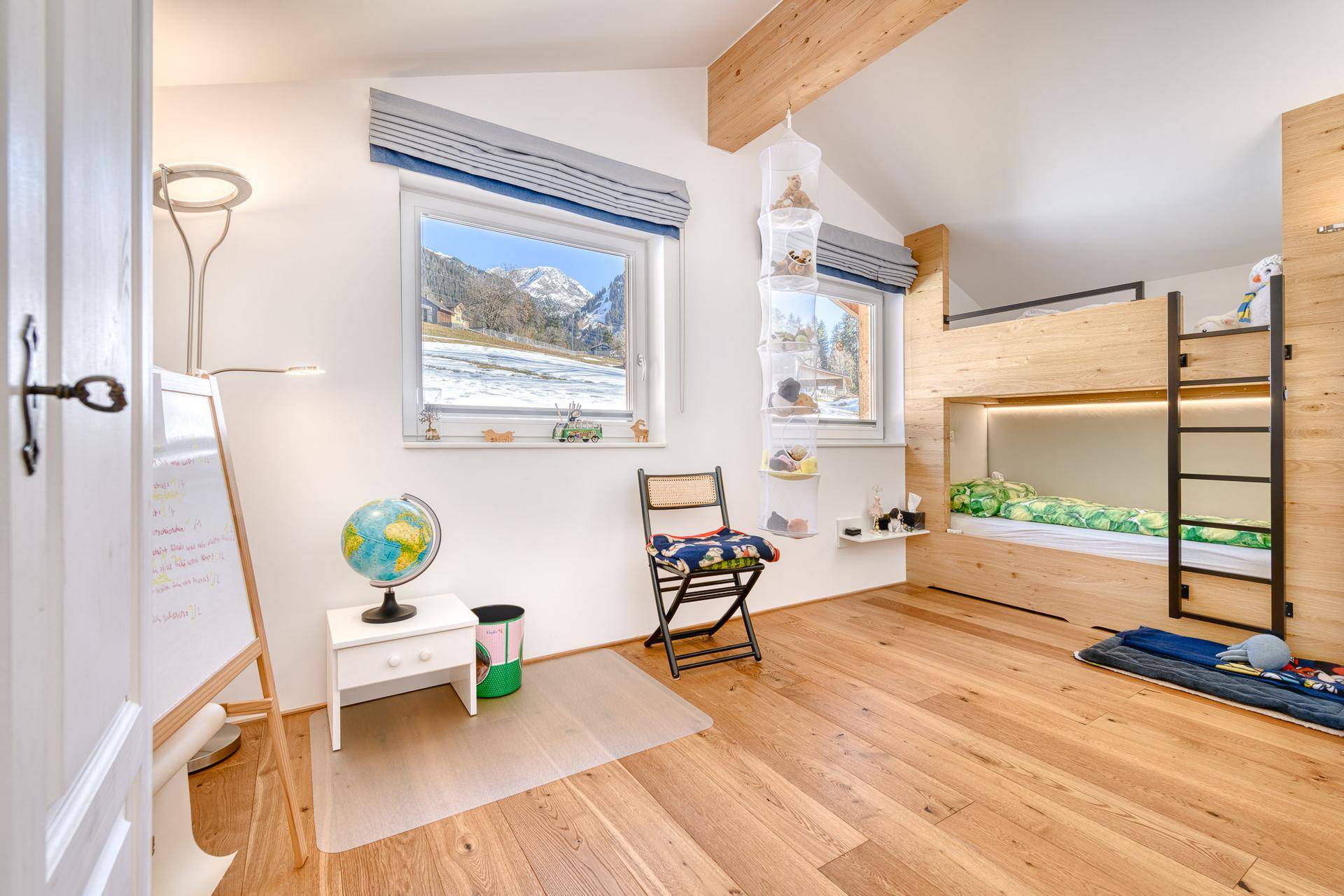 Helles Kinderzimmer mit Etagenbett, Holzboden und Blick auf die verschneite Berglandschaft.