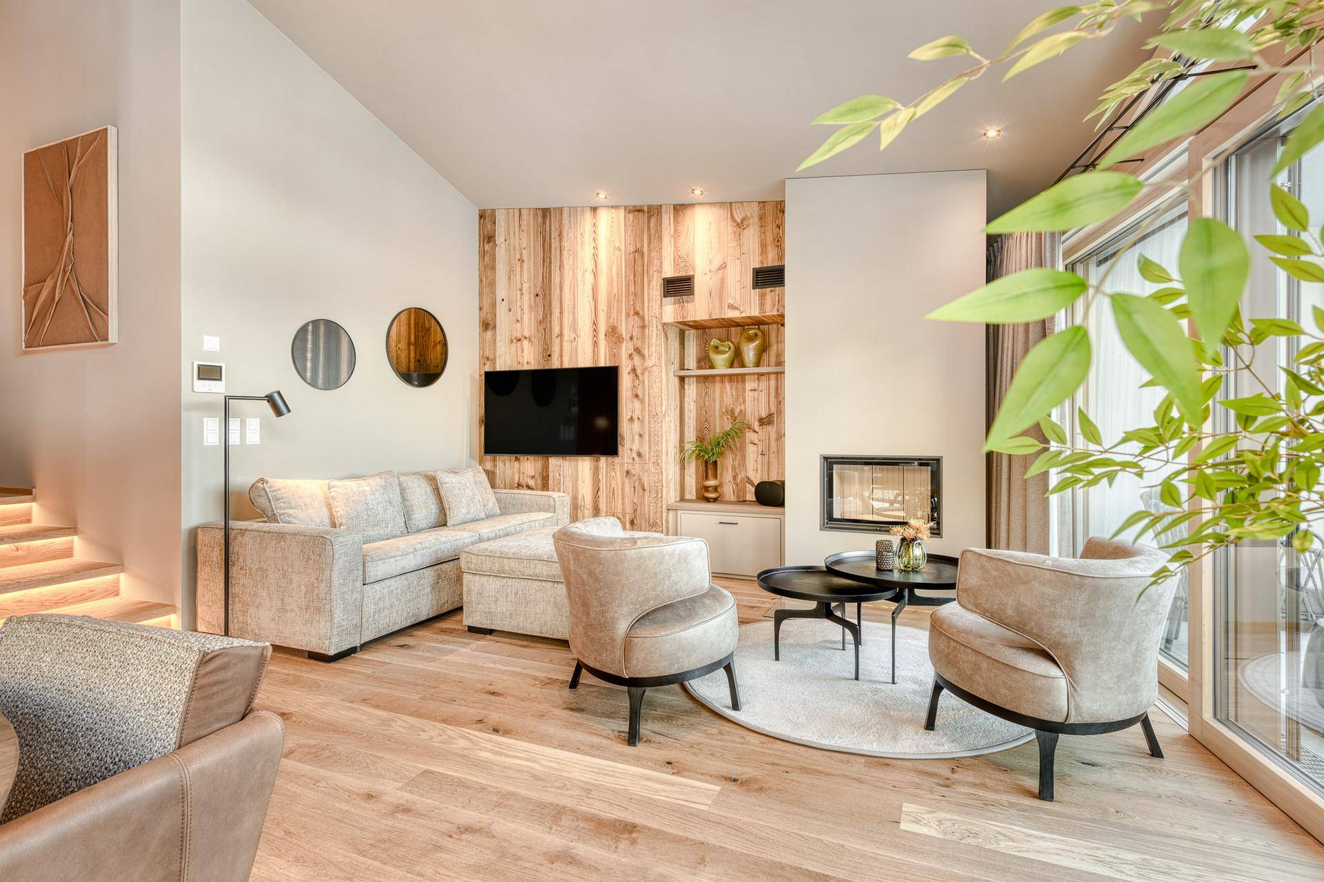 Helles, modernes Wohnzimmer mit Holzakzentwand, Kamin und großen Fenstern mit Blick ins Grüne.