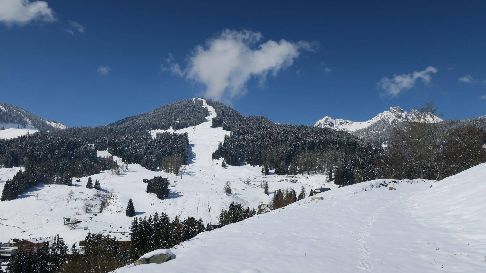 Panoramablick auf eine schneebedeckte Berglandschaft mit Skipisten und einem klaren, blauen Himmel.