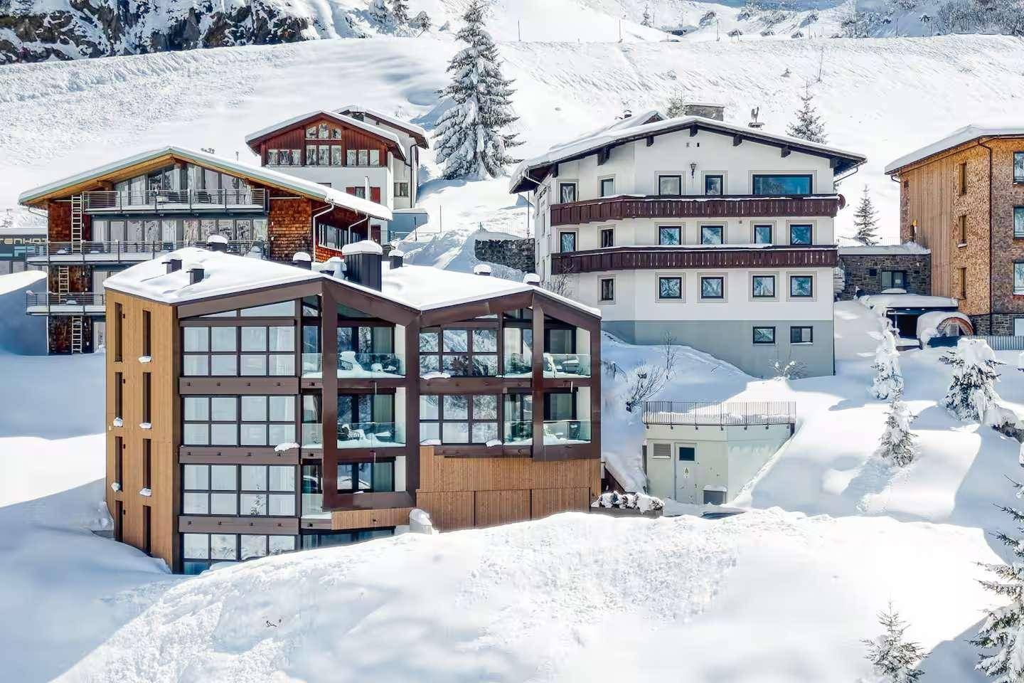 Mehrere moderne und traditionelle Gebäude in einer verschneiten Alpenlandschaft.