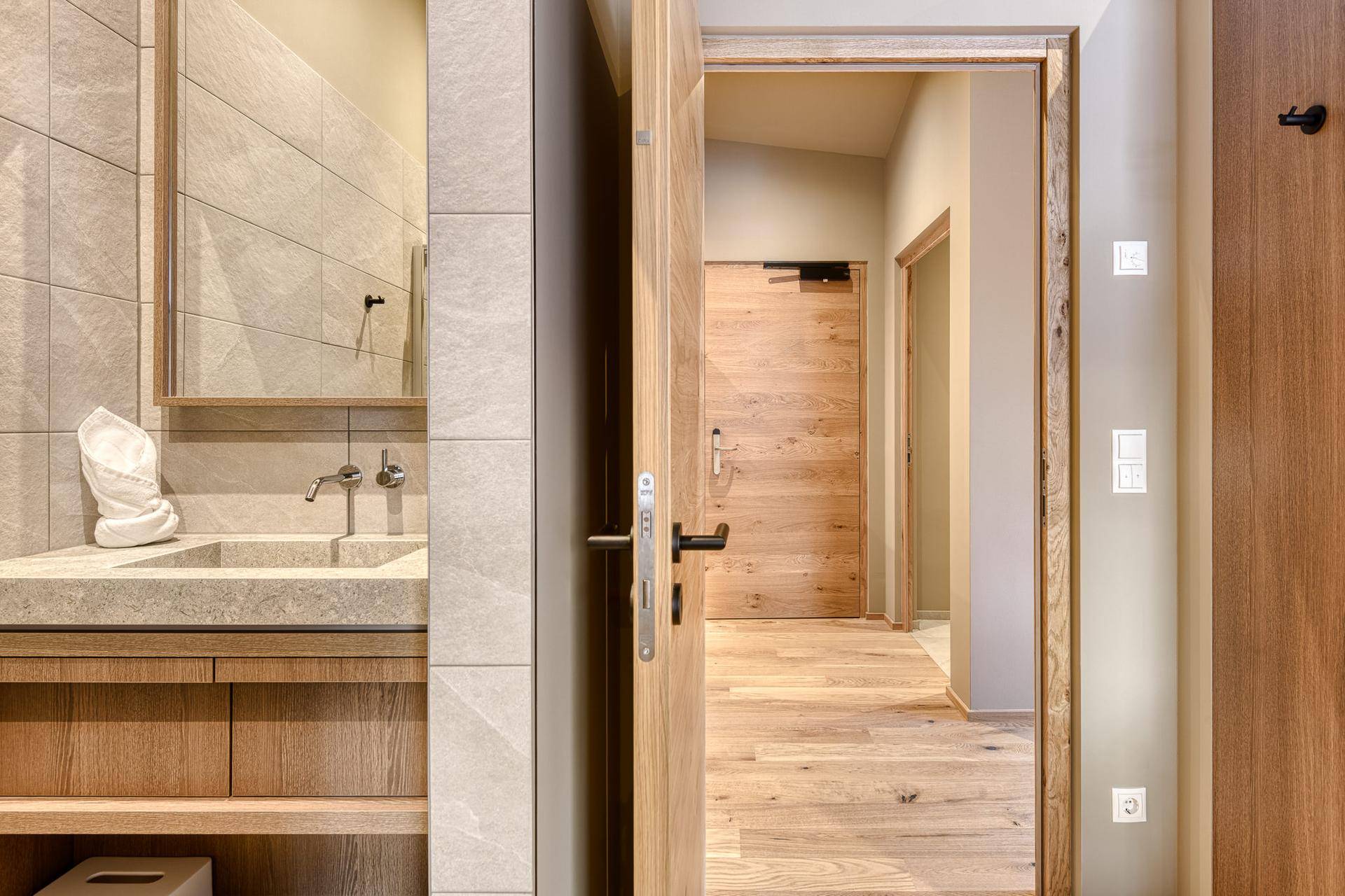 Modernes Badezimmer mit Steinwaschbecken und Holzelementen, angrenzend an einen hellen Flur.