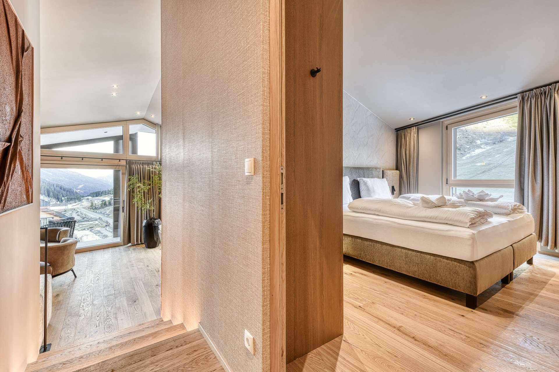 Helles Schlafzimmer mit Doppelbett und Holzboden, mit Blick in den offenen Wohnbereich.