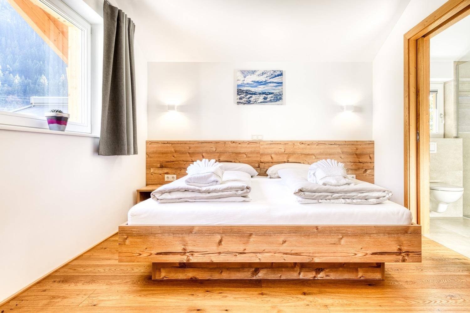 Gemütliches Schlafzimmer mit Doppelbett aus Holz, Holzboden und Bergblick.