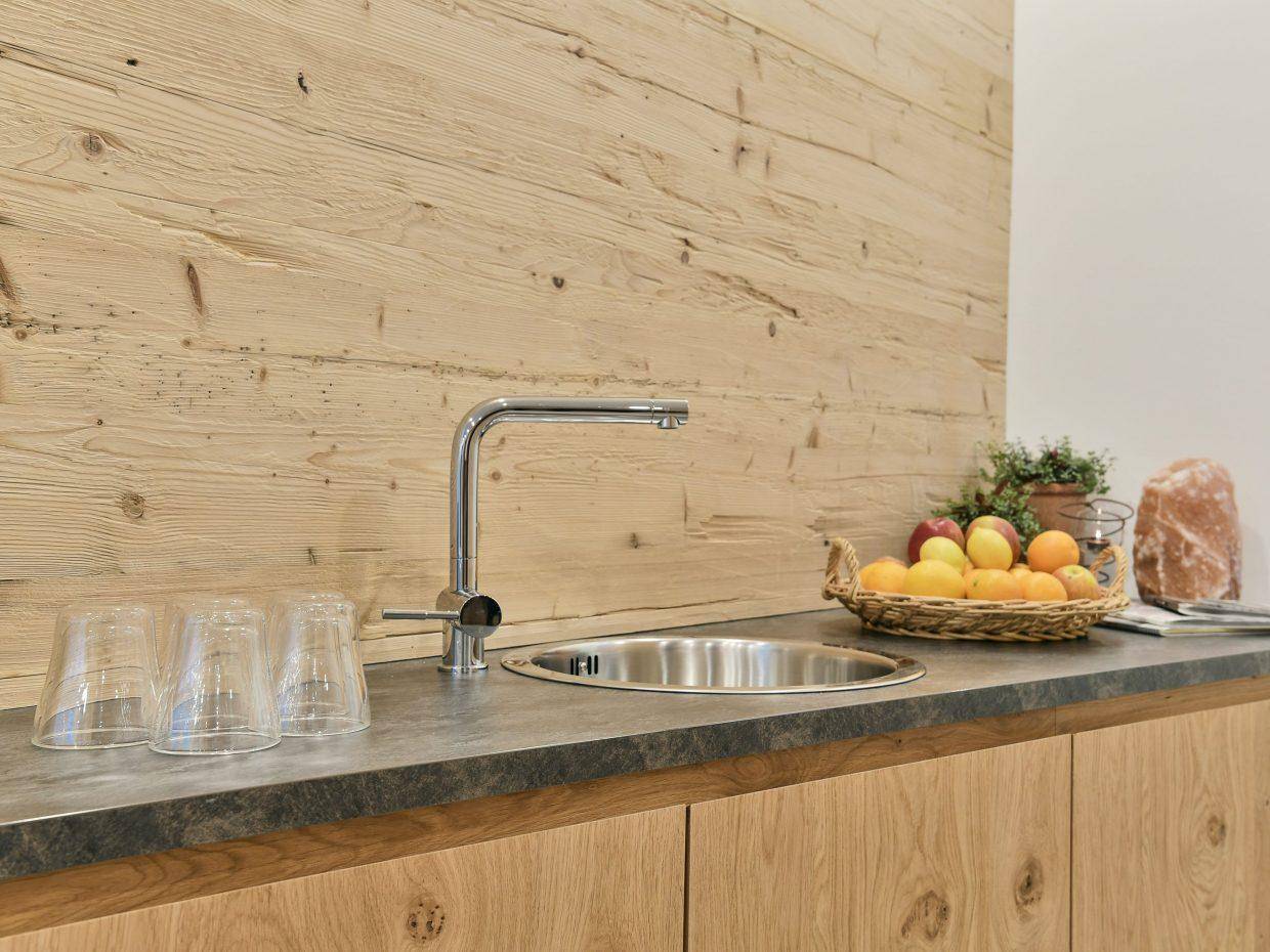 Kleine Küchenzeile mit Holzverkleidung, Spüle und frischem Obst auf der Arbeitsplatte.