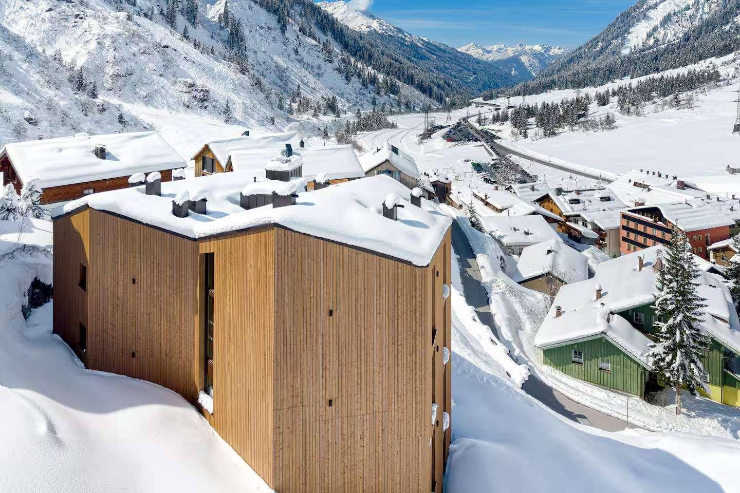 Modernes Holzgebäude mit Flachdach in einer verschneiten Berglandschaft.