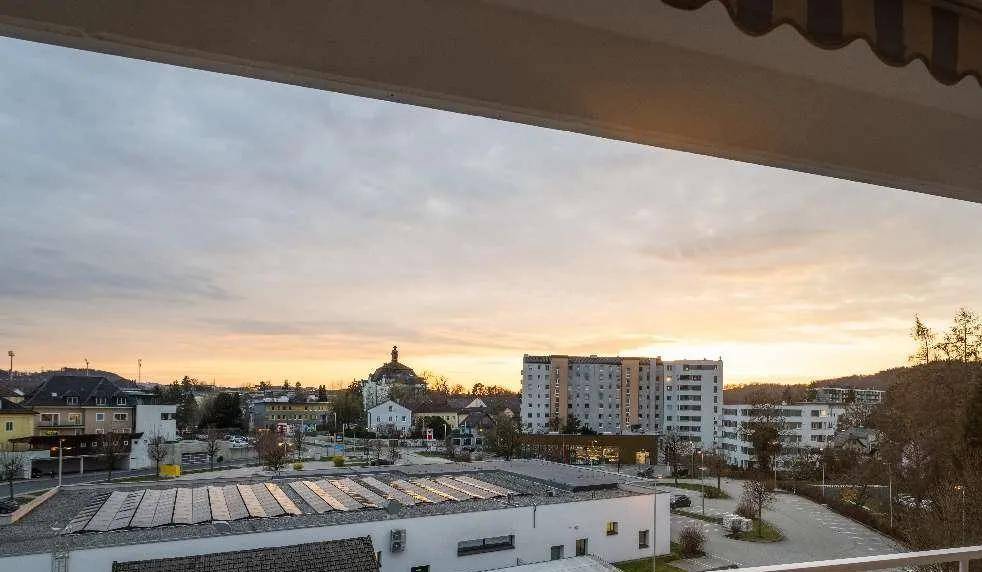 Weitblick vom Balkon über die Stadt bei Sonnenuntergang mit umliegenden Gebäuden.