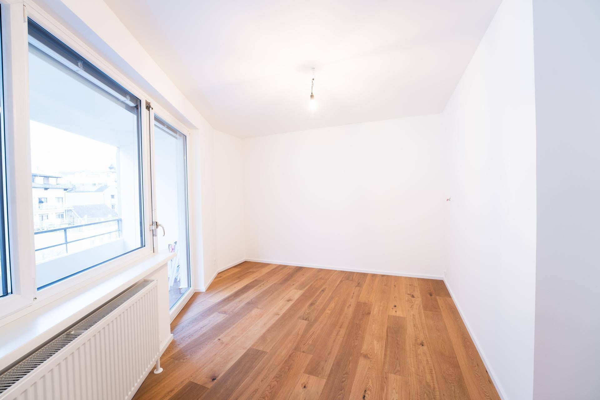 Leerer Raum mit Holzboden und großem Fenster, ideal als Büro oder Schlafzimmer nutzbar.