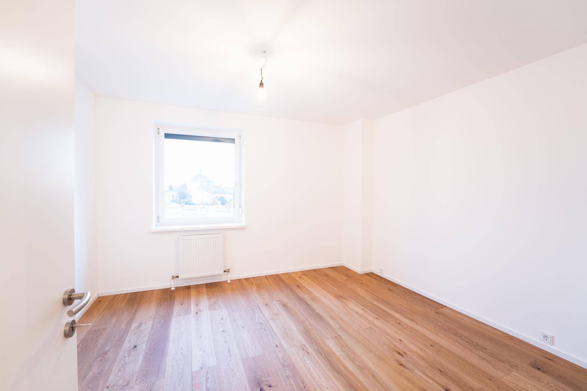 Helles, leeres Schlafzimmer mit Holzboden und Fenster, bereit zur individuellen Gestaltung.