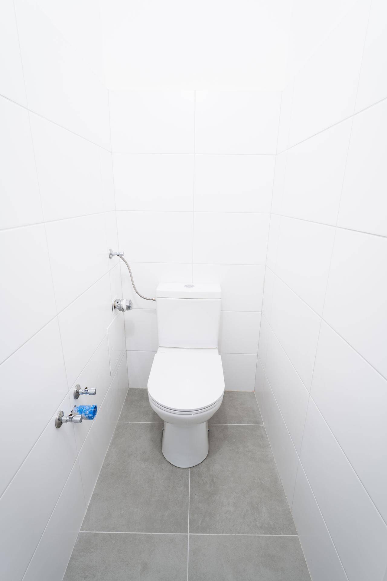 Helles, gefliestes Gäste-WC mit Toilette und Anschlüssen für ein Waschbecken.