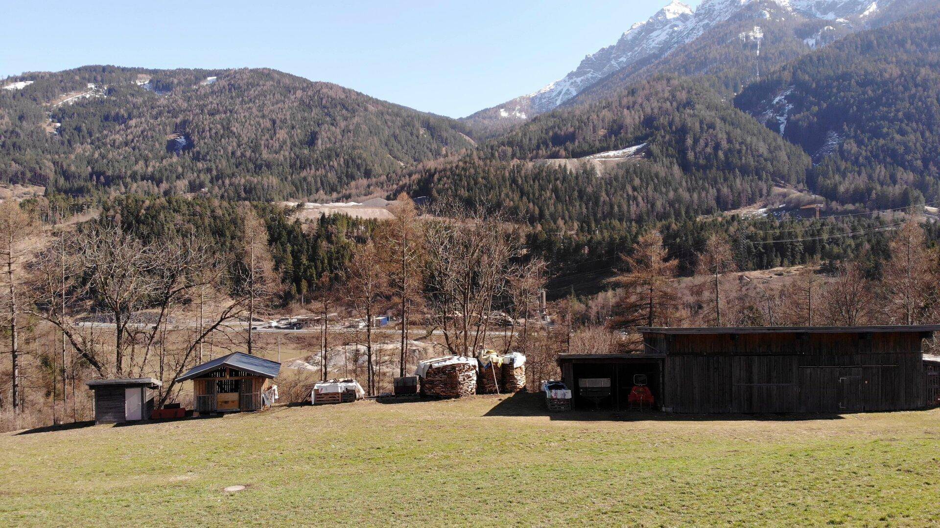 Ländliche Landschaft mit Bergen, Wäldern und kleinen Holzschuppen im Vordergrund.