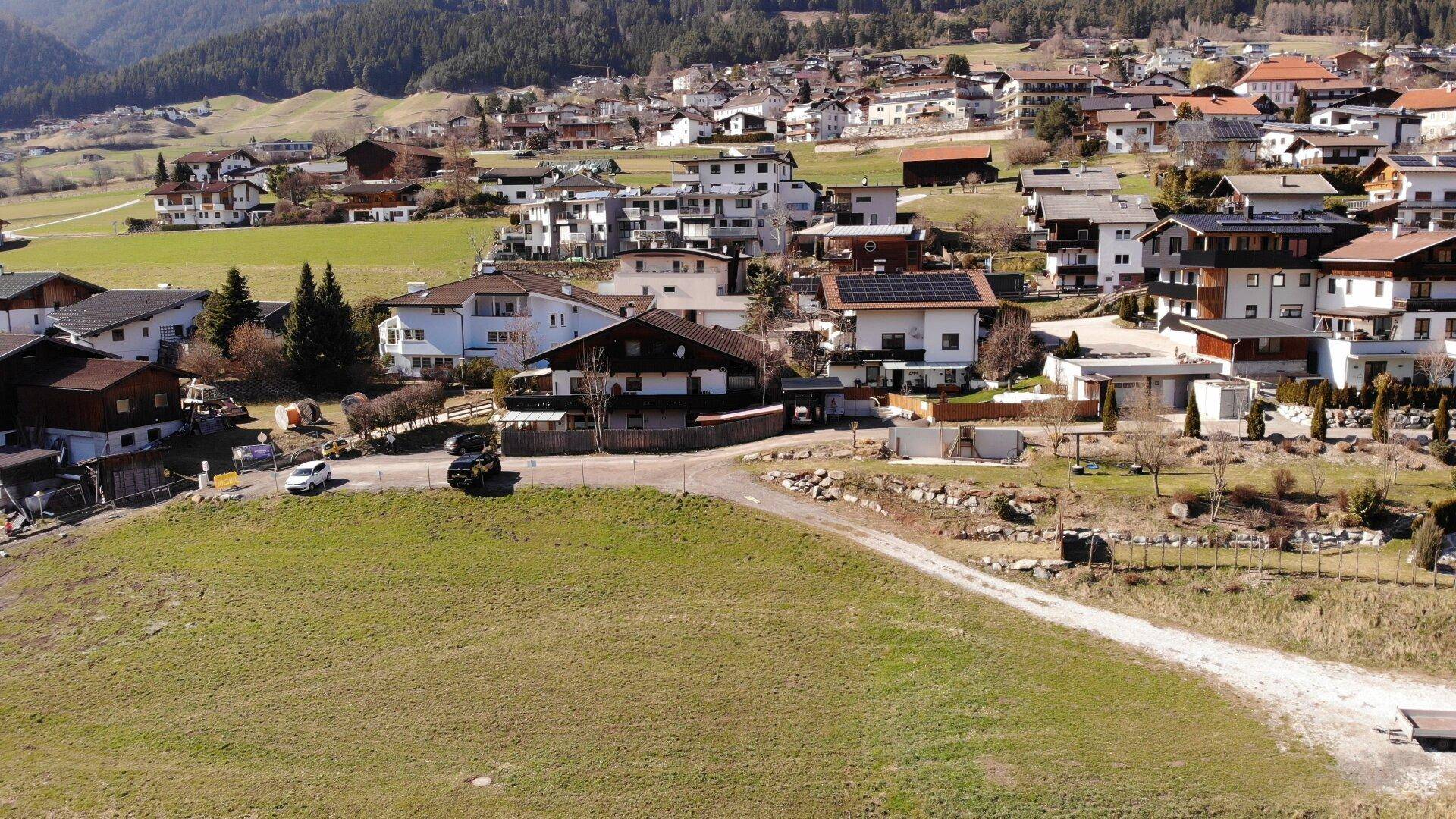 Panoramablick auf ein Dorf mit Wohnhäusern und umliegender Berglandschaft.