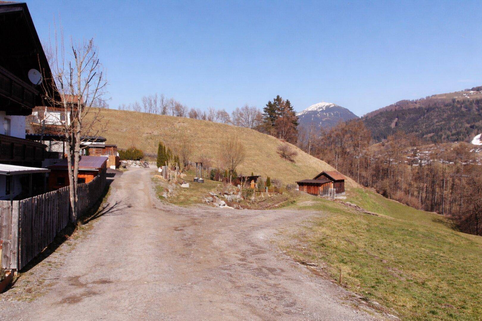 Schotterweg führt einen grünen Hügel hinauf mit Blick auf schneebedeckte Berge.