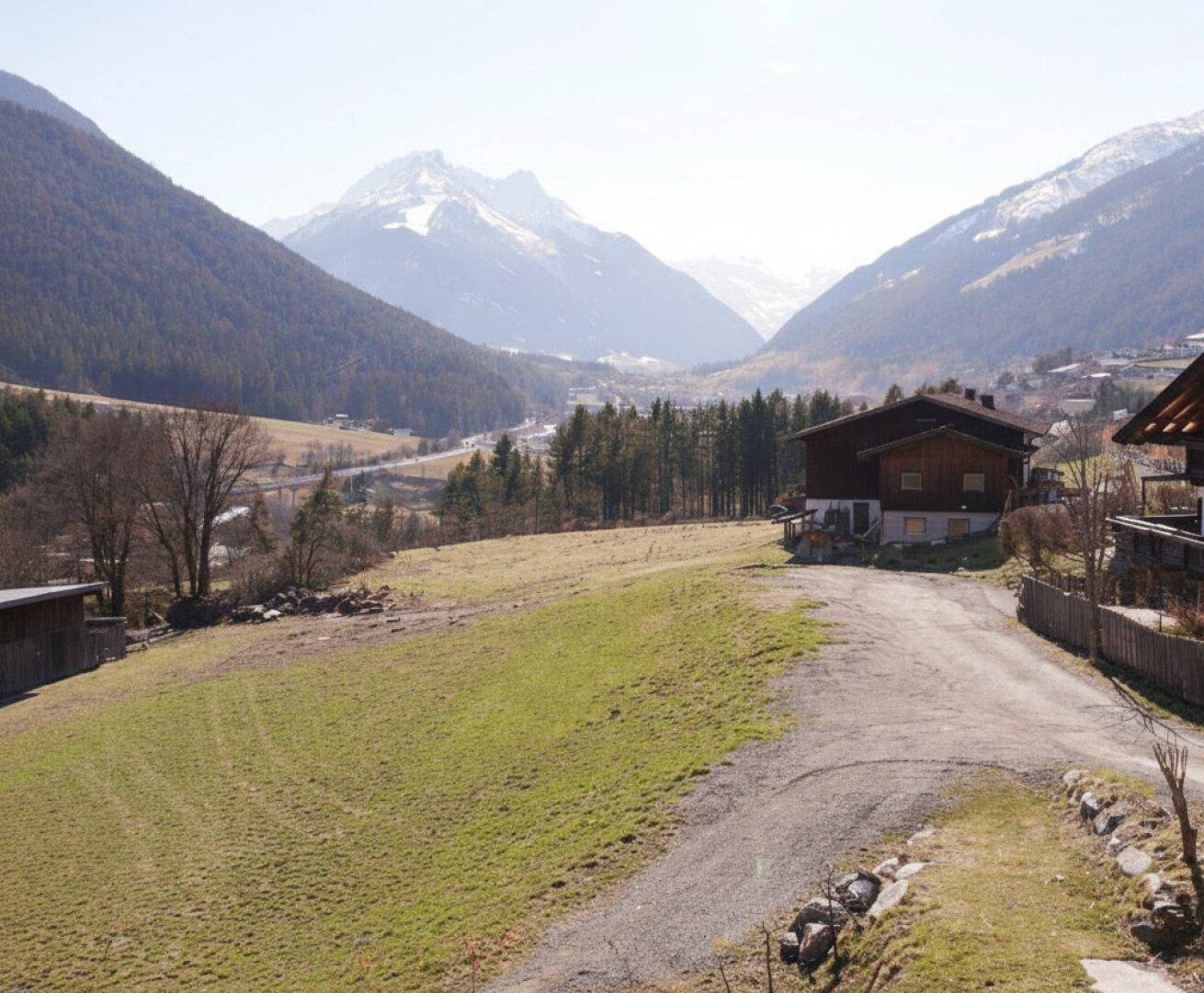 Malerischer Ausblick auf ein Tal mit Bergen, Wäldern und einem traditionellen Haus.