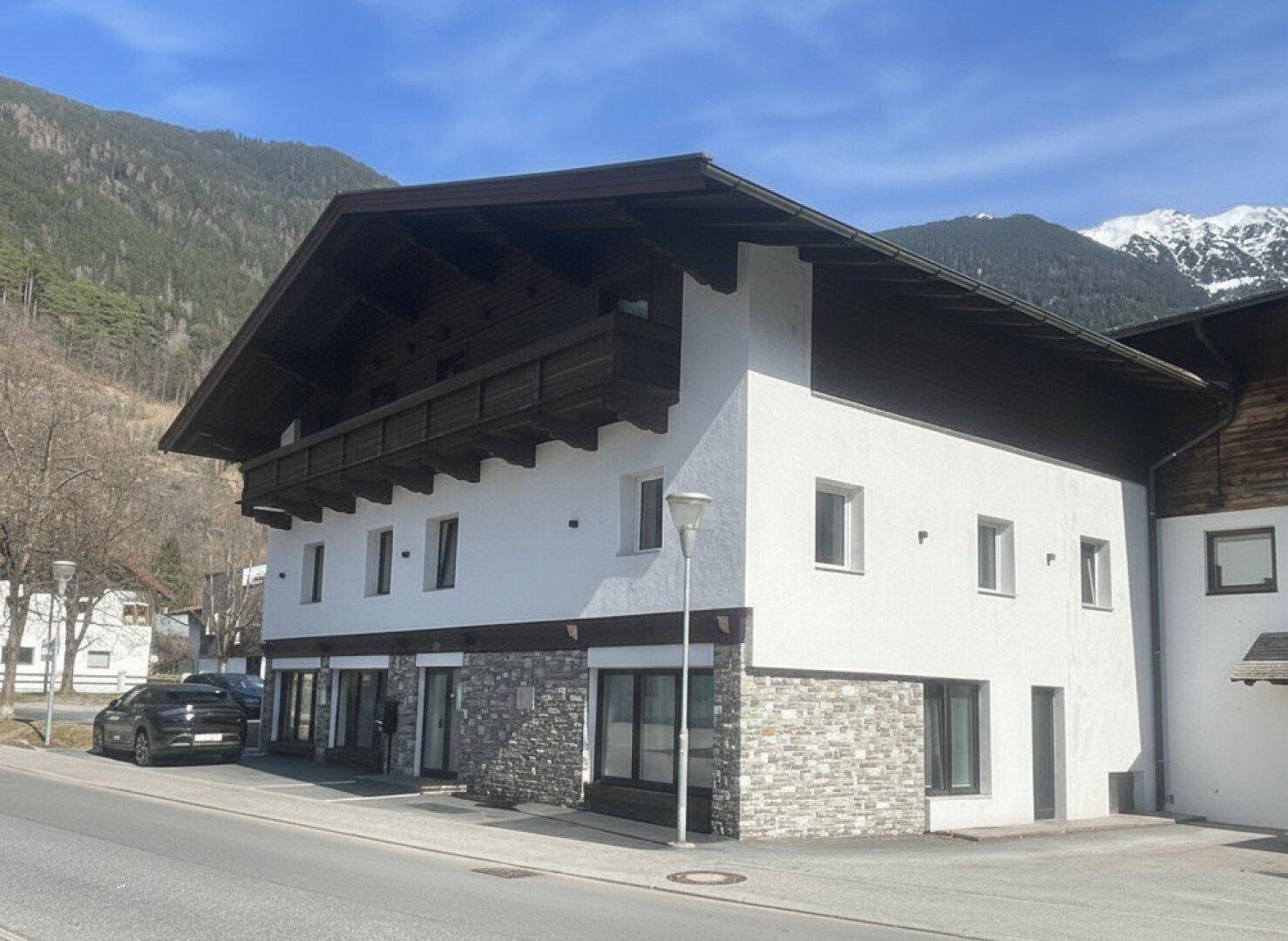 Seitenansicht des Gebäudes mit alpiner Architektur, Holzbalkonen und weißer Putzfassade.