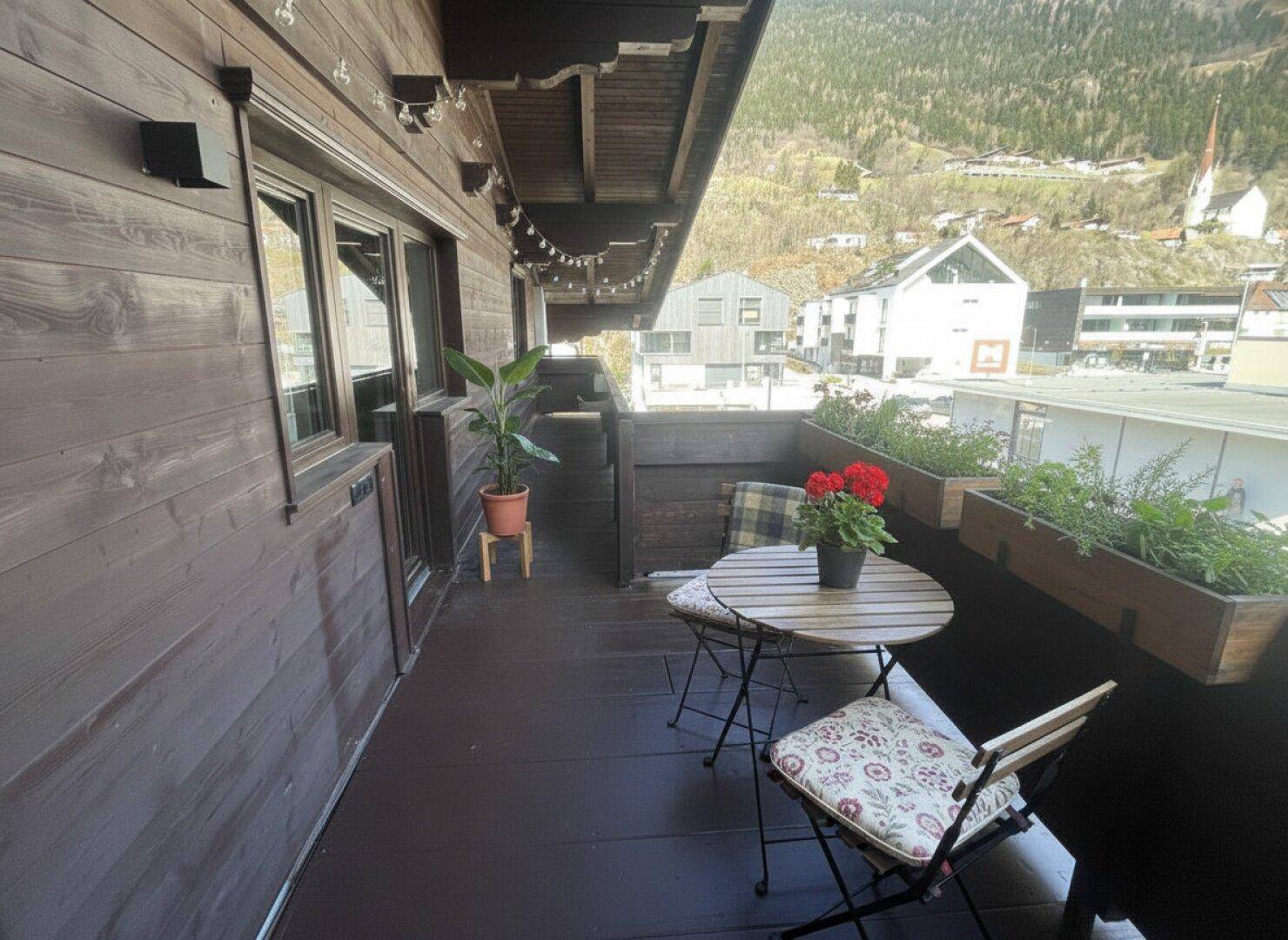 Möblierter Holzbalkon mit Blumenkästen und Blick auf die umliegende Berglandschaft.