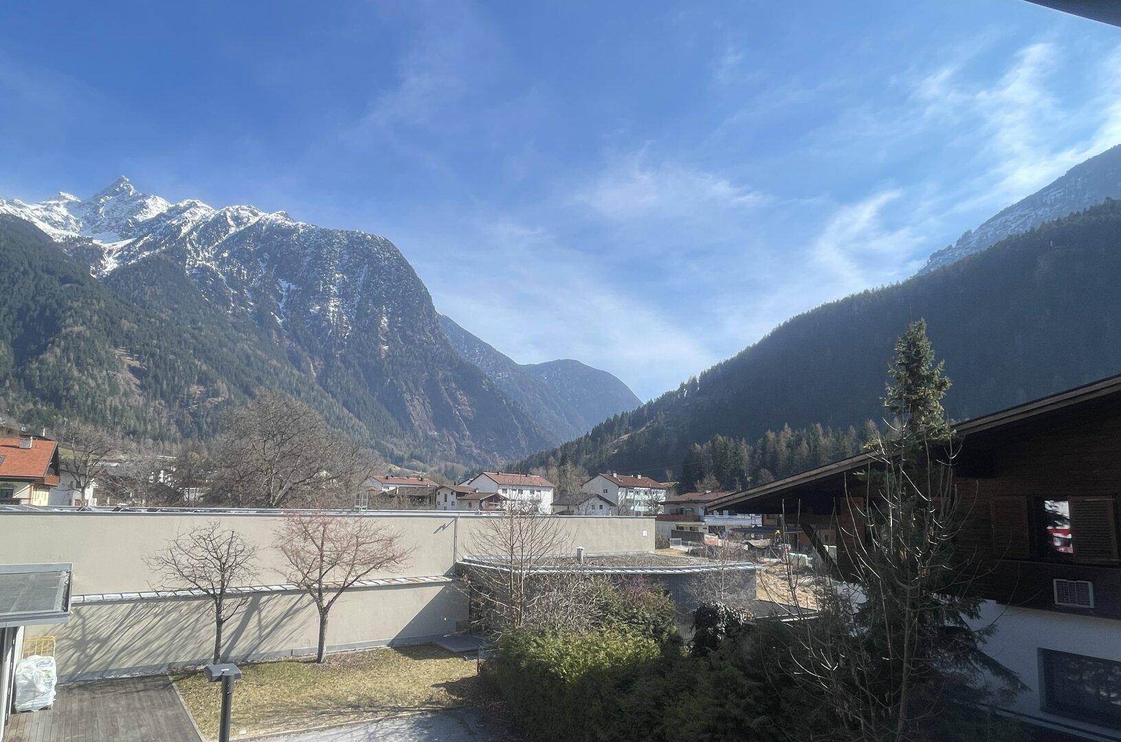 Weitläufiger Blick auf die umliegende Berglandschaft und das Tal unter blauem Himmel.