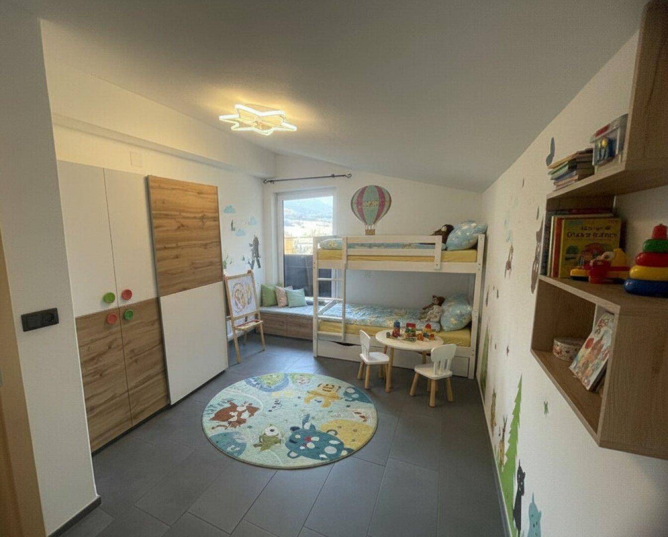 Kinderzimmer mit Etagenbett, Spielbereich und farbenfroher Wanddekoration unter Dachschräge.