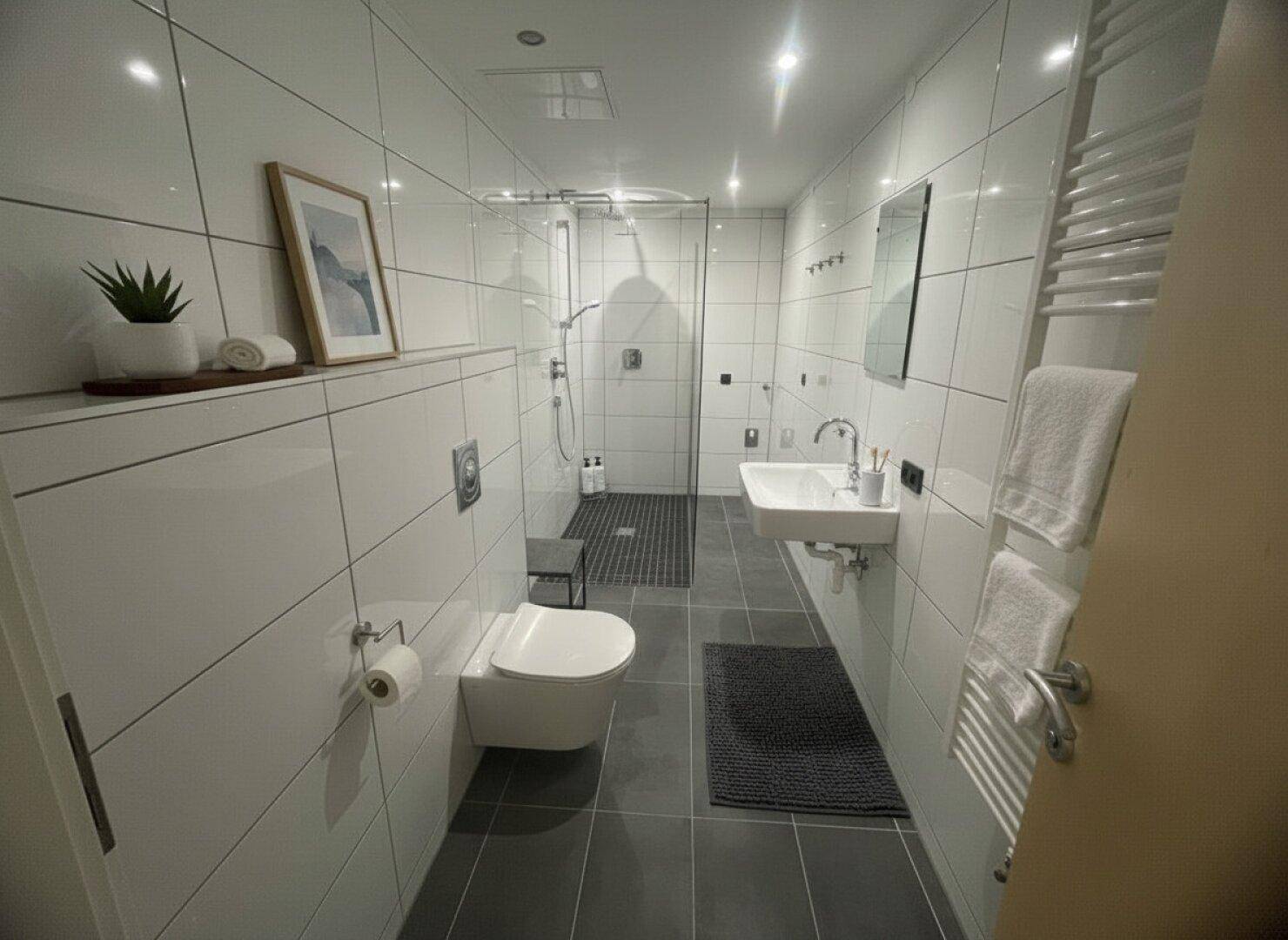 Modernes Badezimmer mit weißen Fliesen, ebenerdiger Dusche und beheiztem Handtuchhalter.