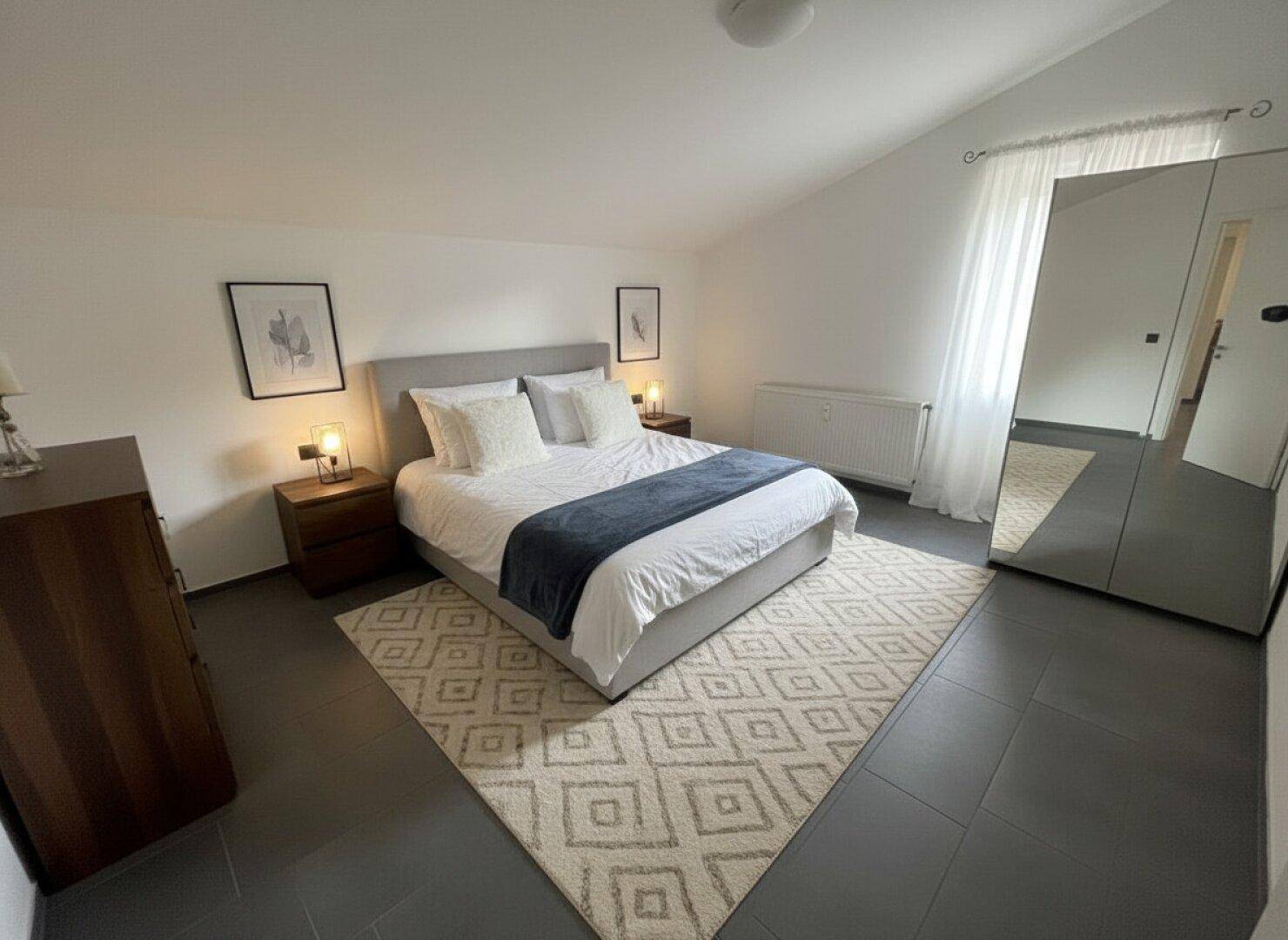 Helles Schlafzimmer mit Doppelbett, Teppich und Spiegelschränken unter Dachschräge.