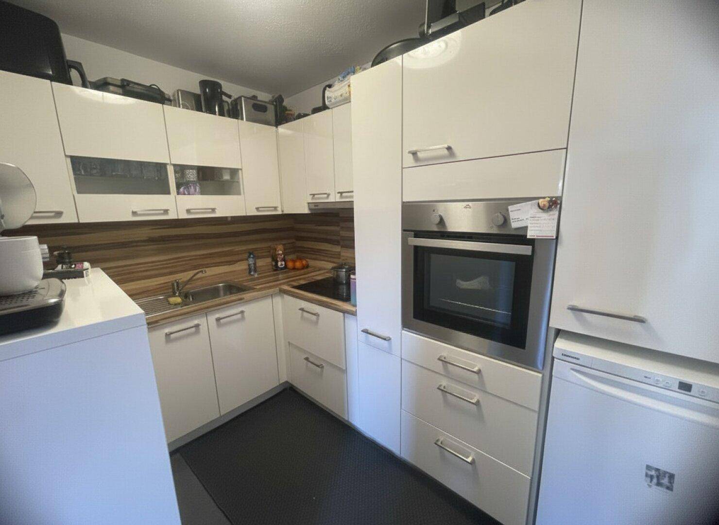 Moderne weiße Einbauküche mit Hochglanzfronten, integriertem Backofen und viel Stauraum.