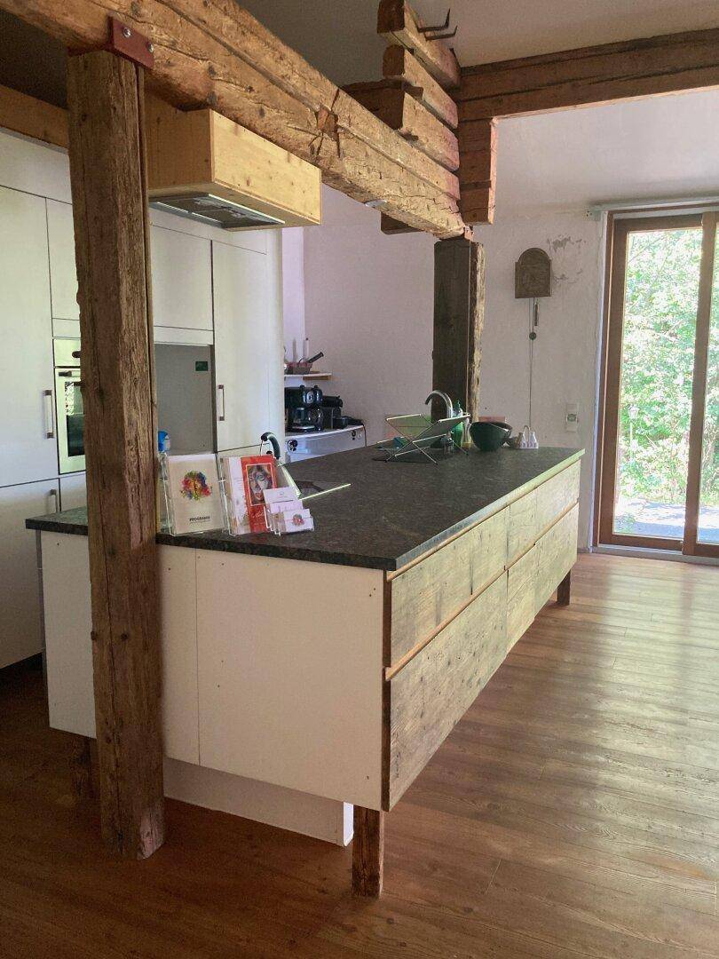 Moderne Küche mit Kücheninsel, dunkler Arbeitsplatte und rustikalen Holzbalken, mit Zugang zum Garten.