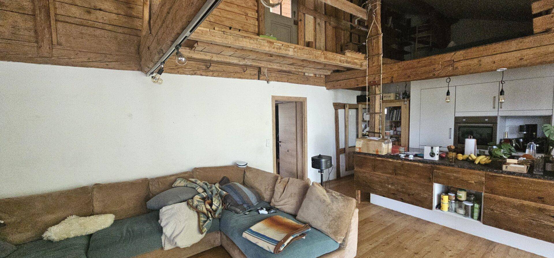 Gemütlicher Wohnbereich mit großem Sofa, sichtbaren Holzbalken und offener Verbindung zur Küche.