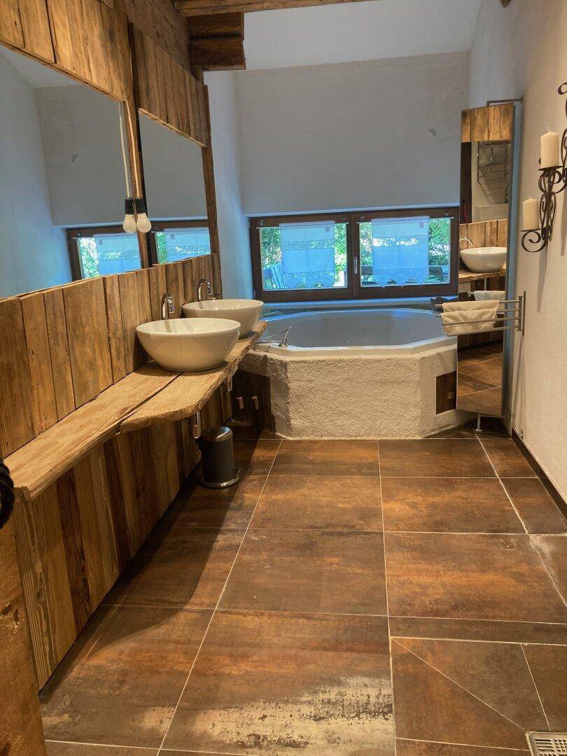 Helles Badezimmer mit Eckbadewanne, zwei Aufsatzwaschbecken und Holzdetails, gut beleuchtet.