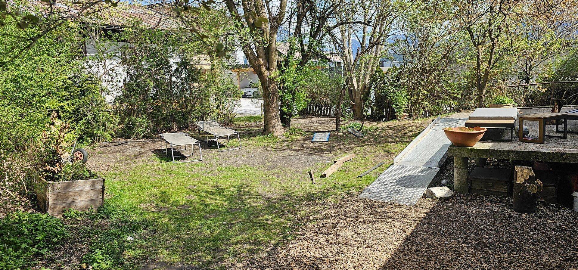 Naturbelassener Gartenbereich mit Rasenfläche, Bäumen und einer Rampe, bereit zur Gestaltung.