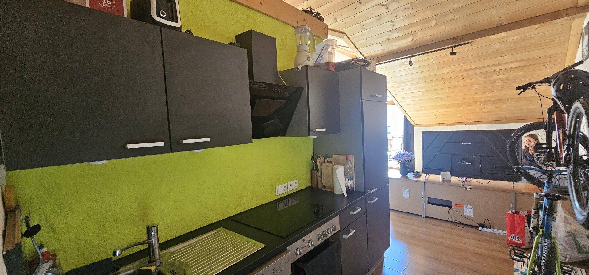 Kleine Küche im Dachgeschoss mit grüner Wand, schwarzen Schränken und schrägen Decken.