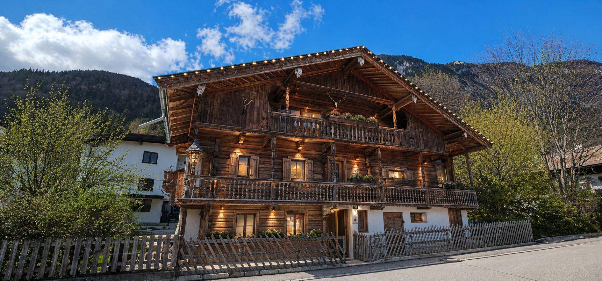 Charmantes Holzhaus im alpinen Stil mit mehreren Balkonen und traditionellen Verzierungen vor einer Bergkulisse.