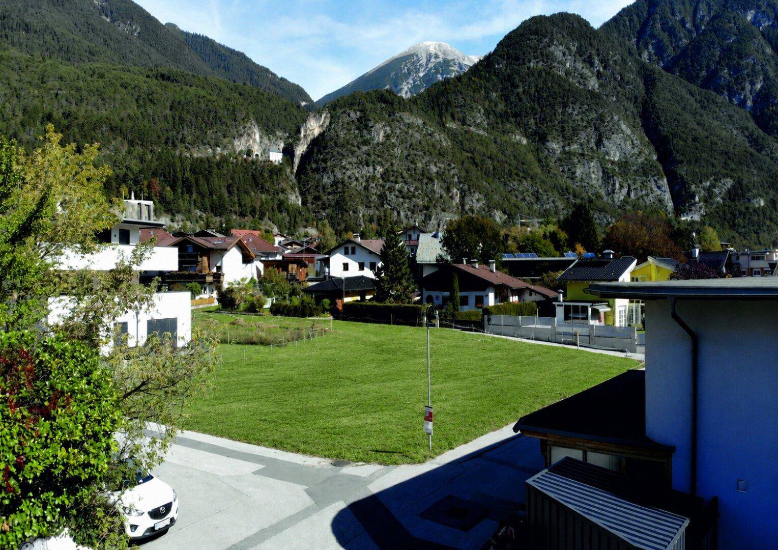 Weitläufige Grünfläche mit umliegenden Häusern und beeindruckendem Bergblick.