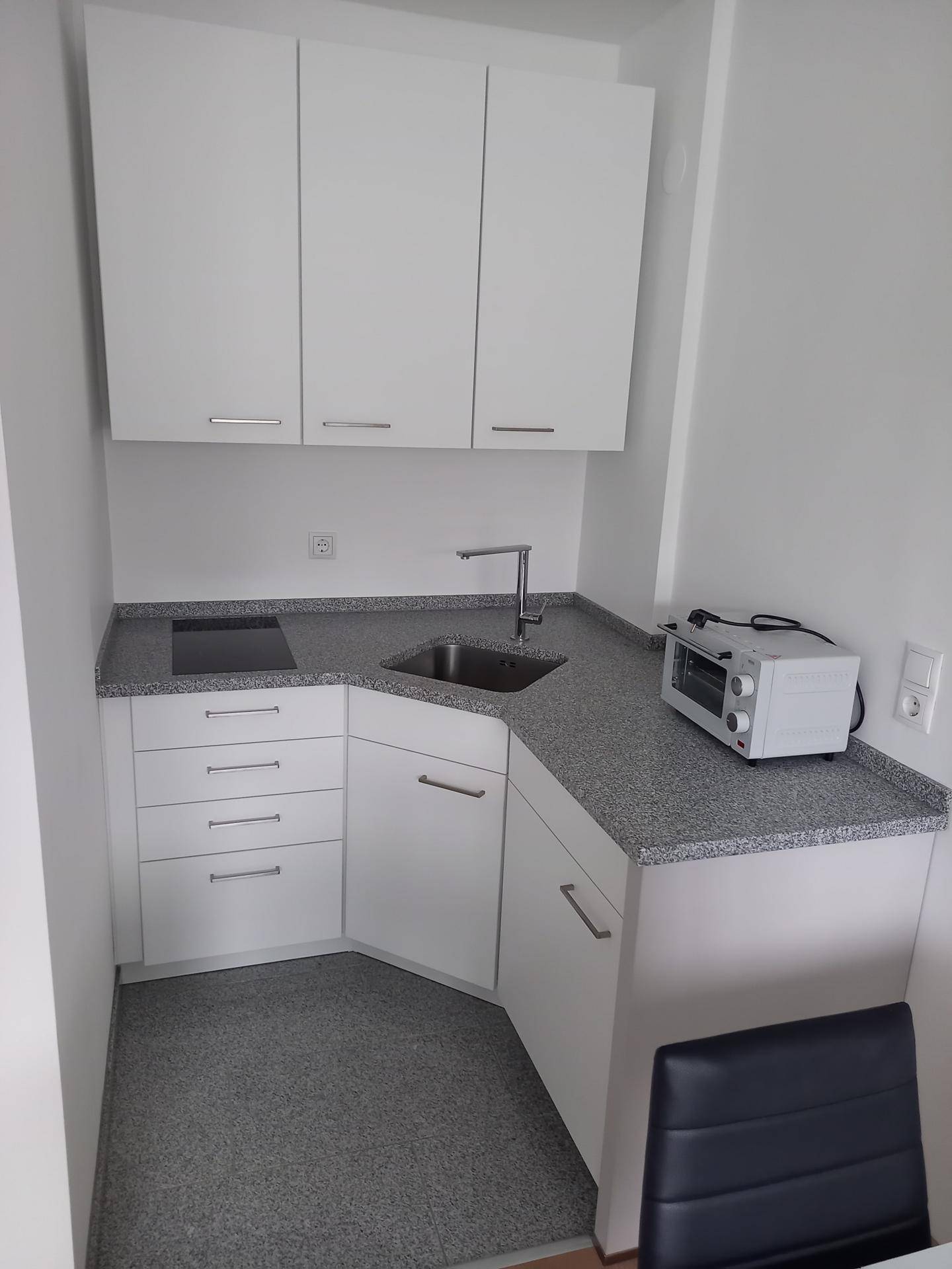 Funktionale Küchenzeile mit weißen Schränken, Induktionskochfeld und Granit-Arbeitsplatte.