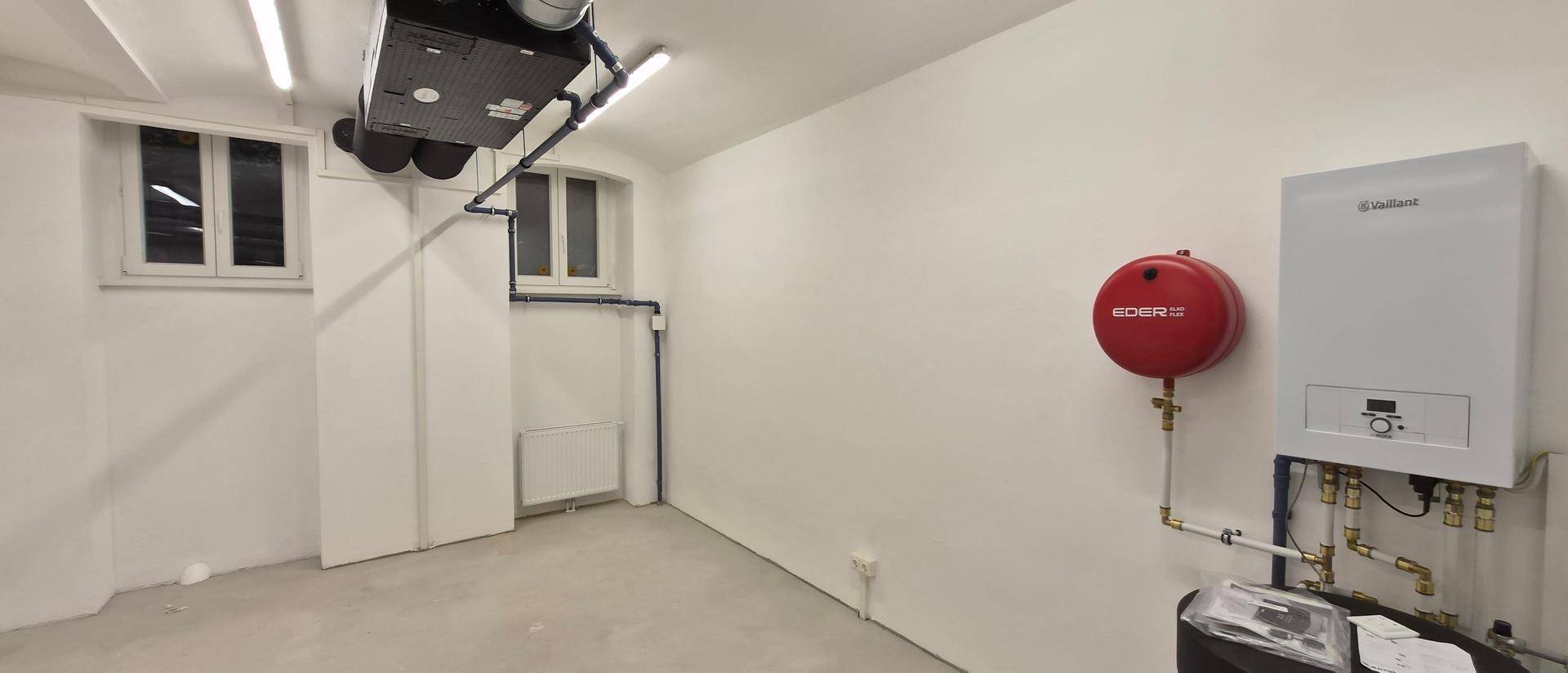 Technikraum mit Heizungsanlage, Warmwasserspeicher und Lüftungssystem an der Decke.