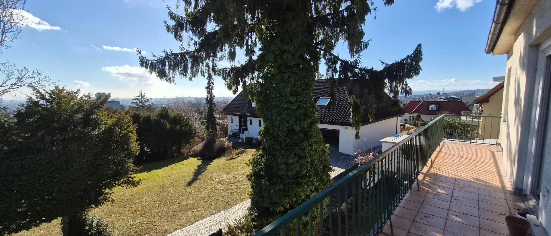 Geräumiger Balkon mit Fliesenboden und weitem Blick über den Garten und die Stadt in der Ferne.