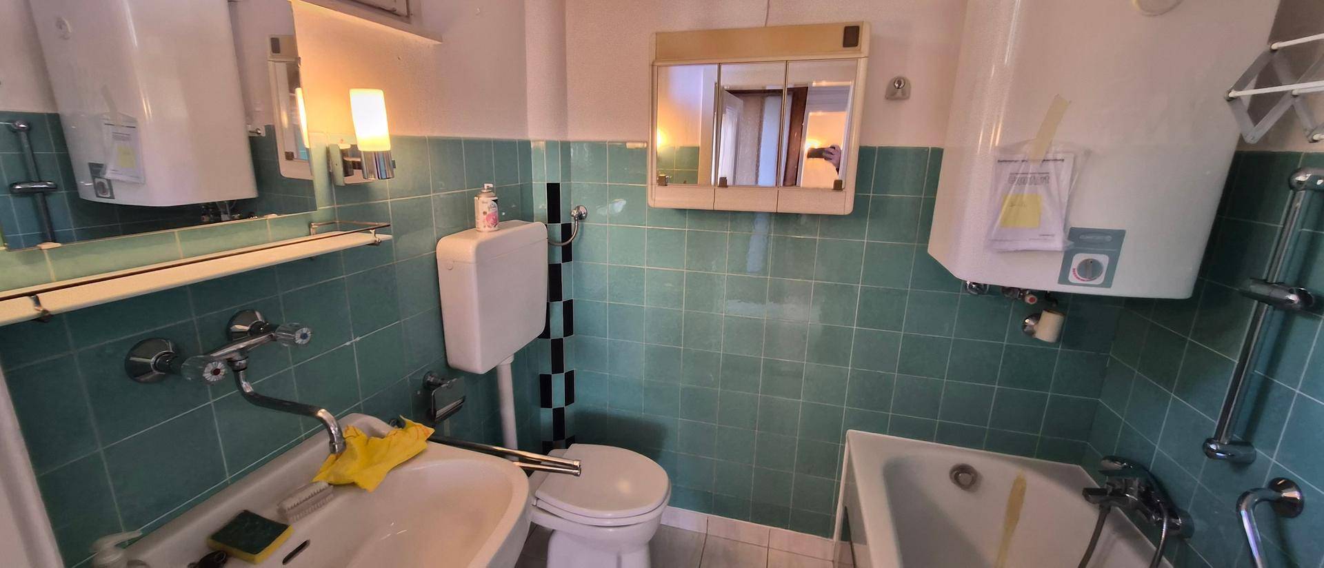Badezimmer mit hellblauen Fliesen, Badewanne und Waschbecken, ausgestattet mit einem Spiegelschrank.