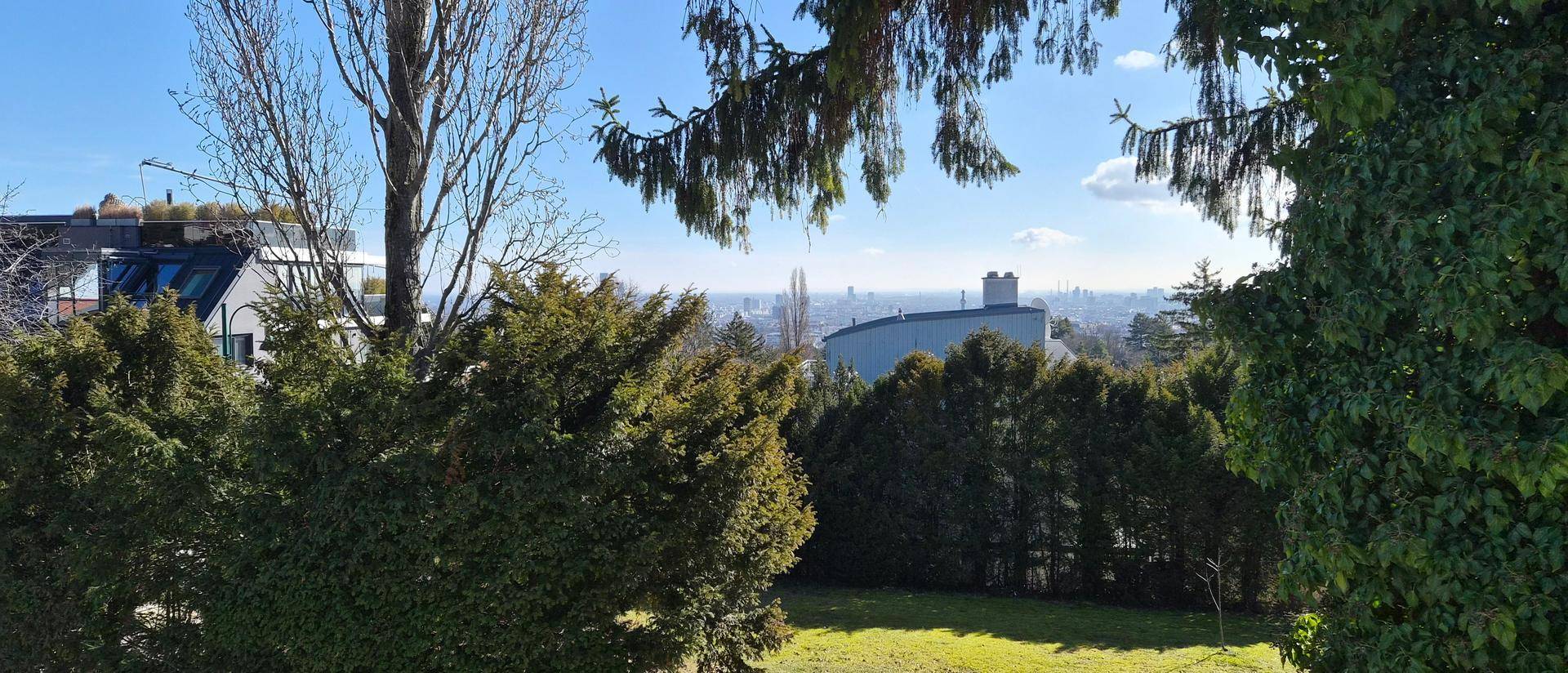 Panoramablick vom Balkon über grüne Hecken und Bäume bis zur fernen Stadtkulisse.
