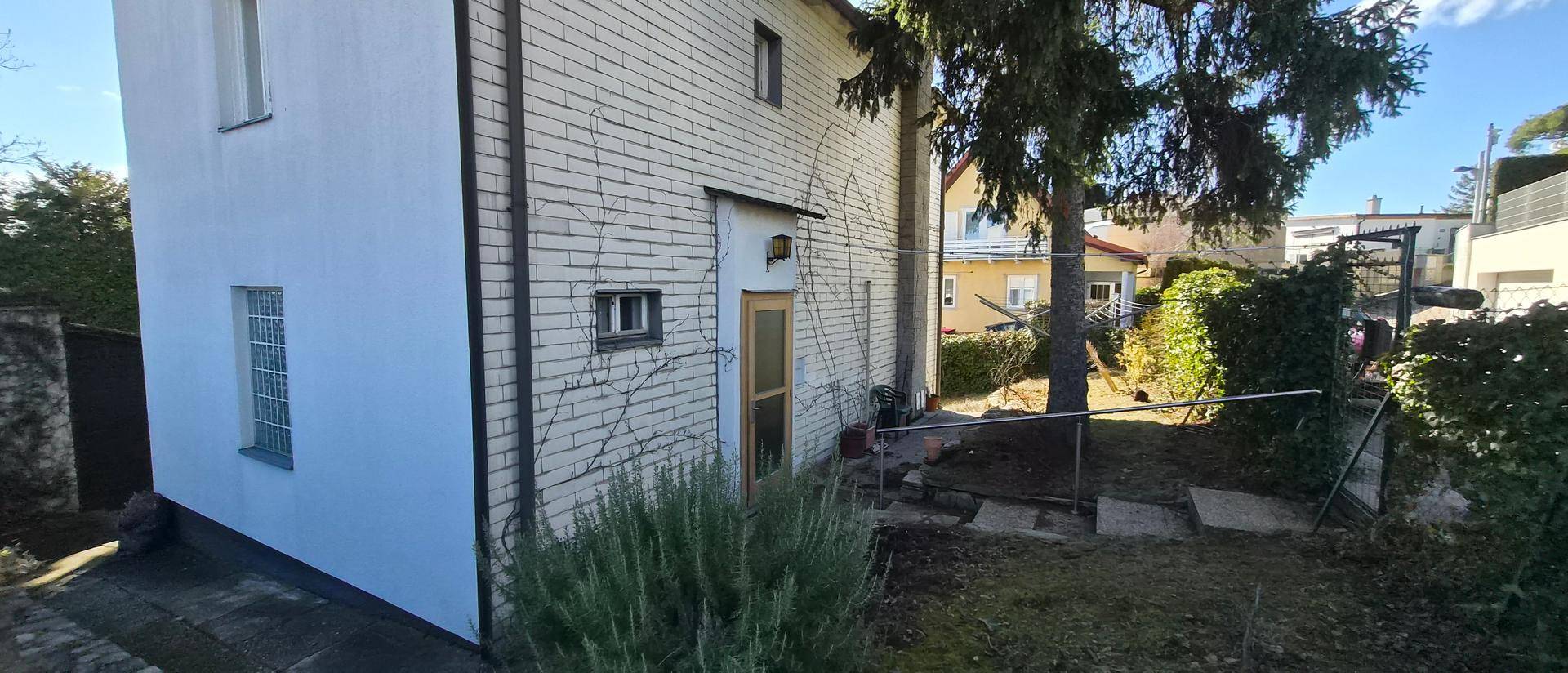 Seitenansicht des Hauses mit heller Ziegelfassade und einem gepflegten Gartenbereich.