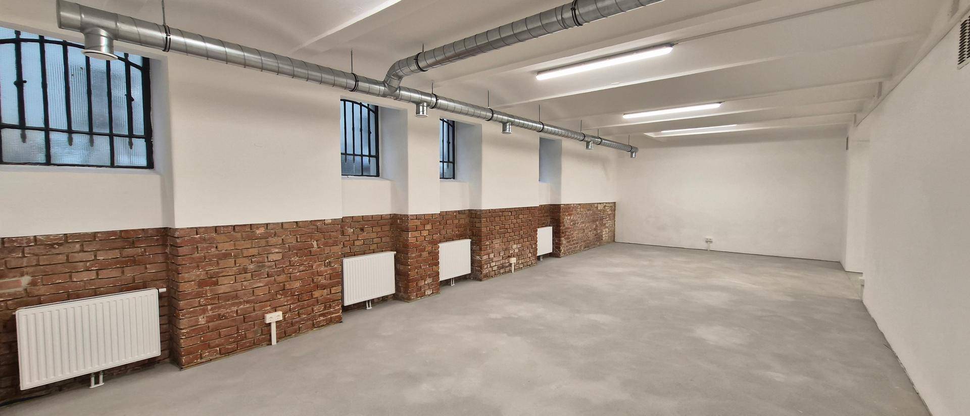 Geräumiger Innenraum mit industriellem Charme, Ziegelmauerwerk und modernen Heizkörpern unter den Fenstern.