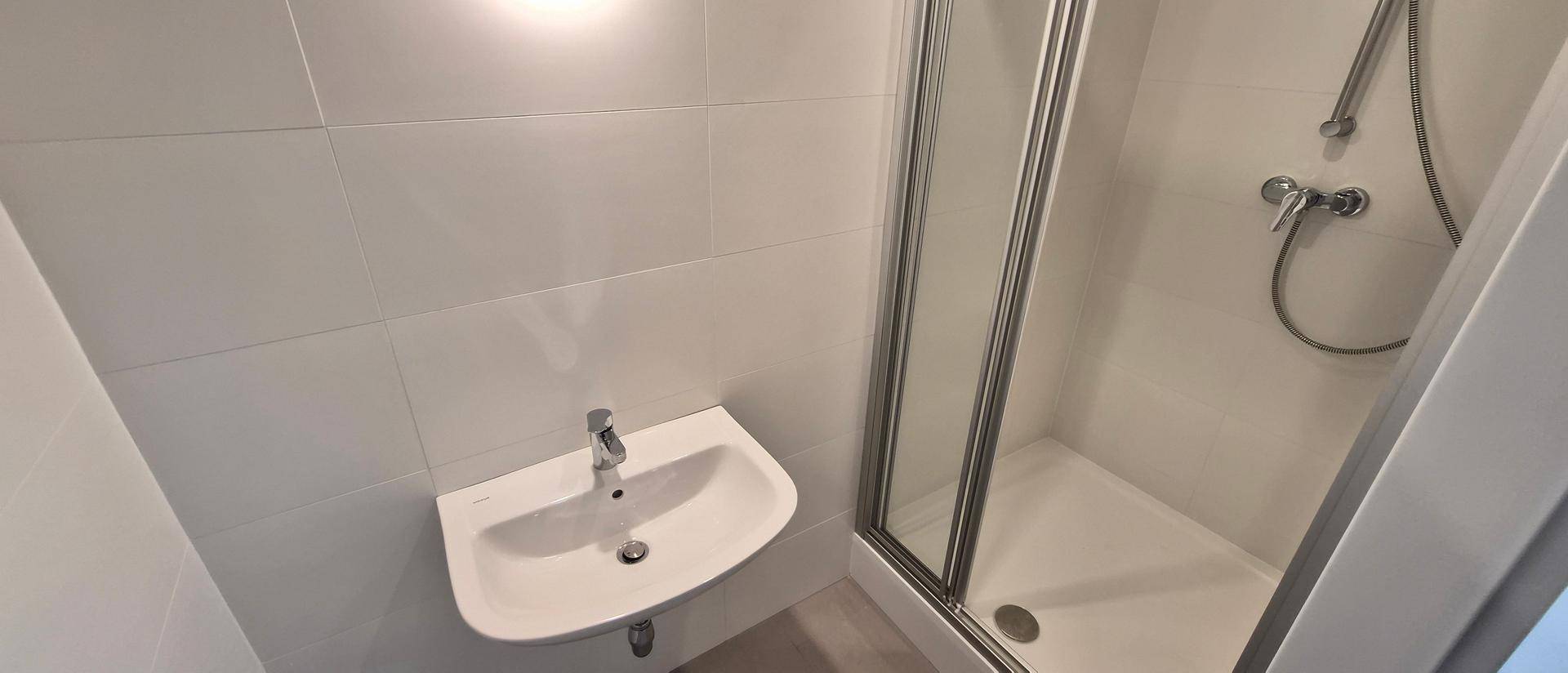 Modernes Badezimmer mit Duschkabine, Waschbecken und weißen Fliesen an den Wänden.