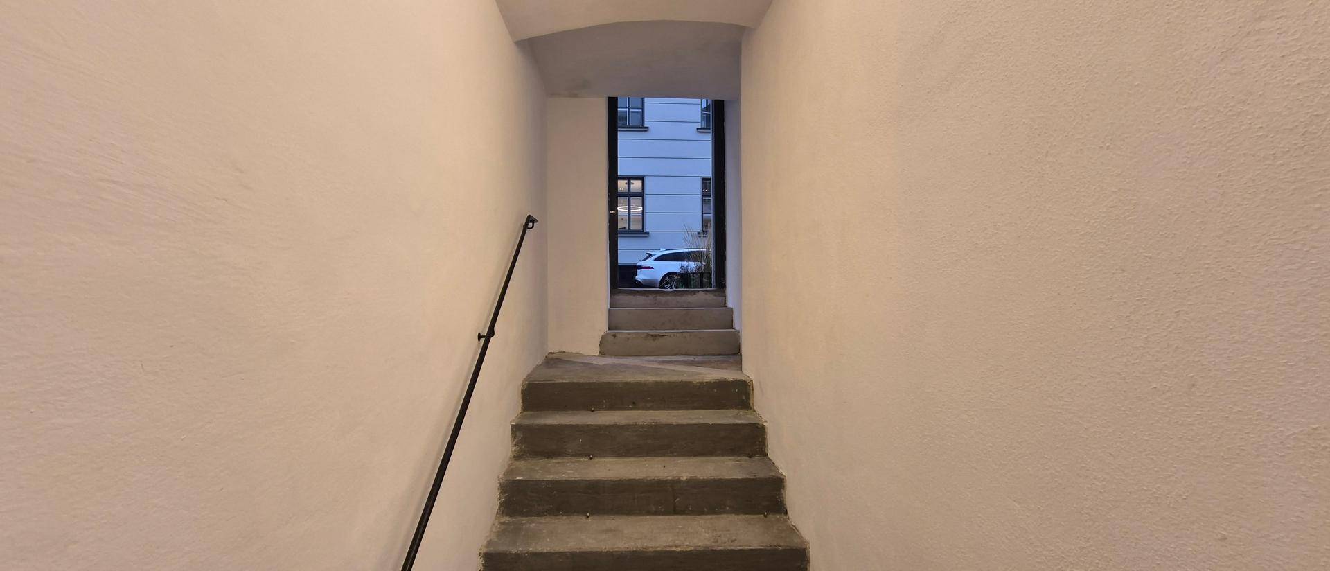 Treppenaufgang mit Handlauf, der zu einem Ausgang mit Blick auf ein geparktes Auto führt.