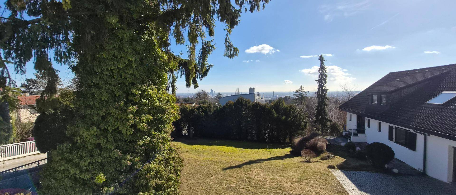 Weitläufiger Blick vom Balkon über einen großen Garten und die Skyline der Stadt am Horizont.