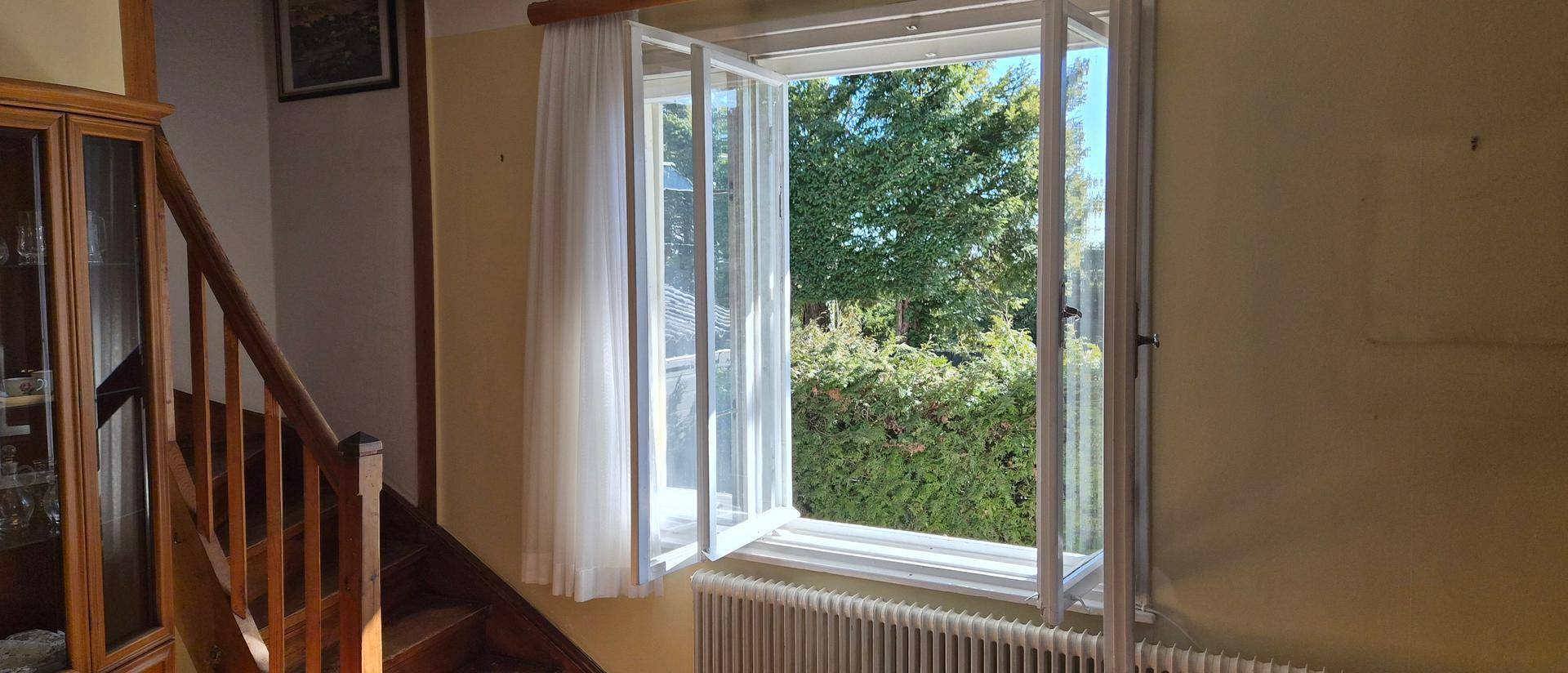 Heller Flurbereich mit Holztreppe und Fenster, das einen Blick auf grüne Hecken bietet.