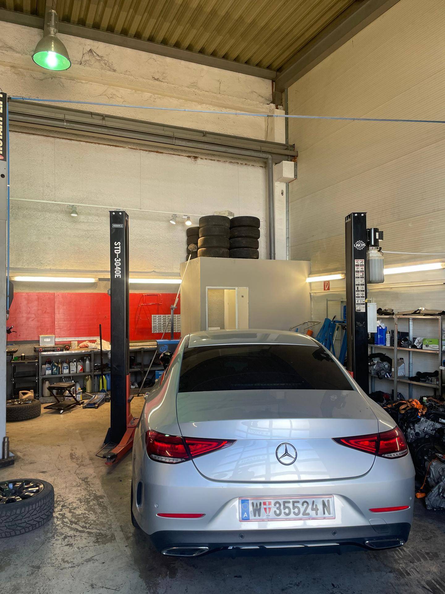 Blick in eine Autowerkstatt mit einem geparkten Fahrzeug, einer Hebebühne und gestapelten Reifen an der Wand.