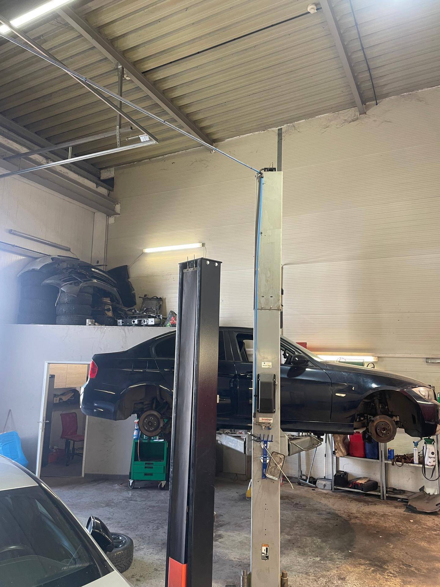 Autowerkstatt mit einem Fahrzeug auf einer Hebebühne und Ersatzteilen, die auf einer erhöhten Lagerfläche gelagert sind.