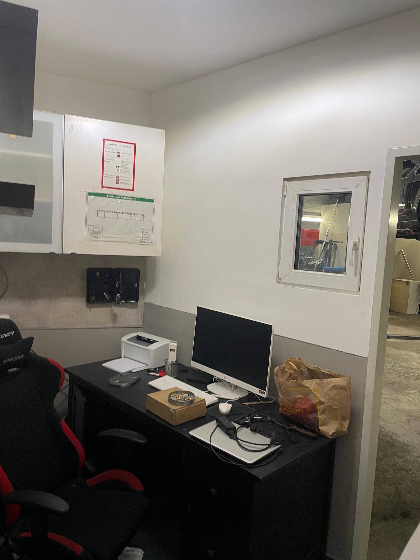 Kompaktes Büro mit Schreibtisch, Computer, Bürostuhl und einem kleinen Fenster, das Tageslicht hereinlässt.